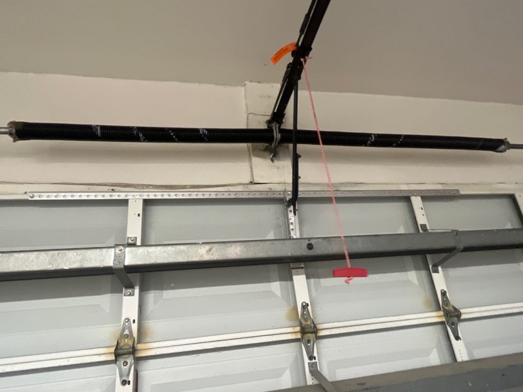 A close-up of a garage door mechanism shows a black torsion spring above the door and a red emergency release cord—highlighting the reliability garage door experts provide for home automation and convenience.