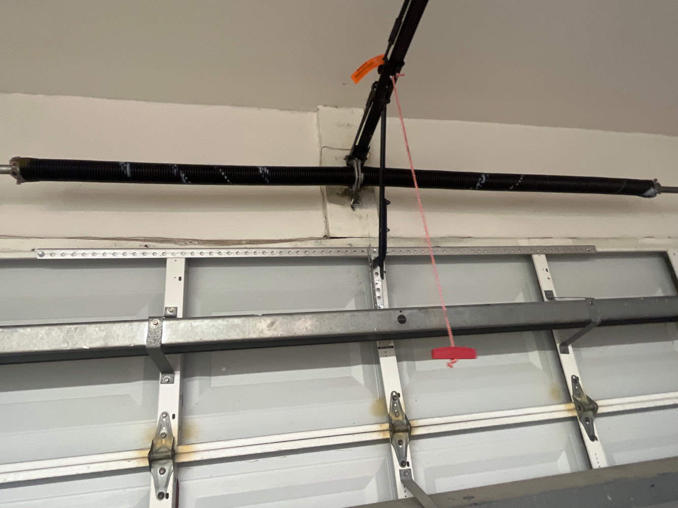 A close-up of a garage door mechanism shows a black torsion spring above the door and a red emergency release cord—highlighting the reliability garage door experts provide for home automation and convenience.