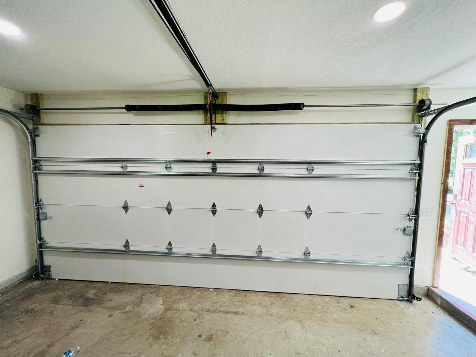 A closed white garage door with metal hinges and tracks, viewed from inside a Hialeah, Florida garage with a concrete floor and beige walls. The segmented garage door sits beside an open doorway to the right.
