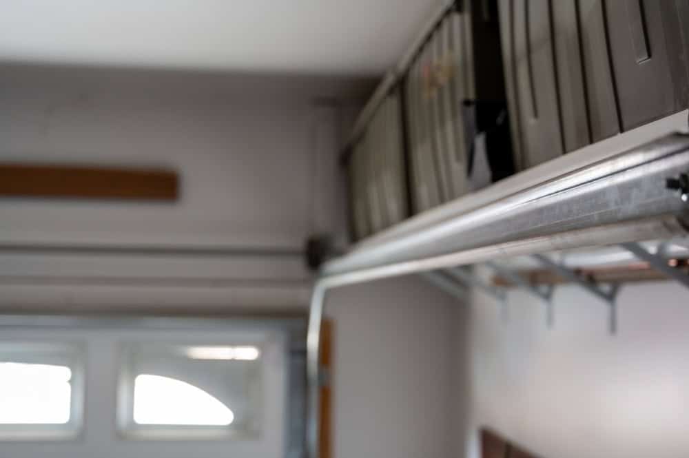 A close-up of a garage interior featuring an open garage door track with storage boxes stacked above it. Some light shines through a small window, softly illuminating the gray walls and ceiling.