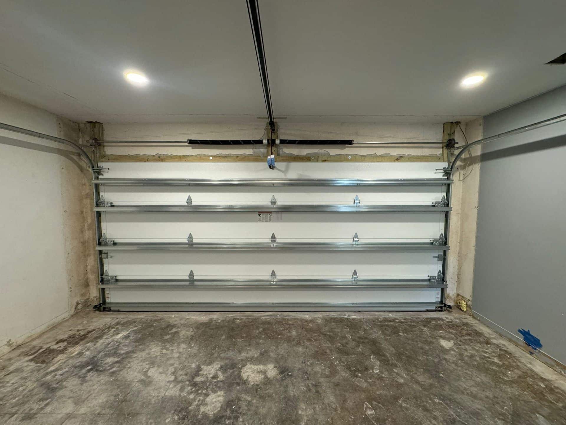 A clean, empty garage in Coral Springs 33065 features a closed metallic sectional garage door, overhead tracks, a concrete floor, and two recessed ceiling lights illuminating the space.