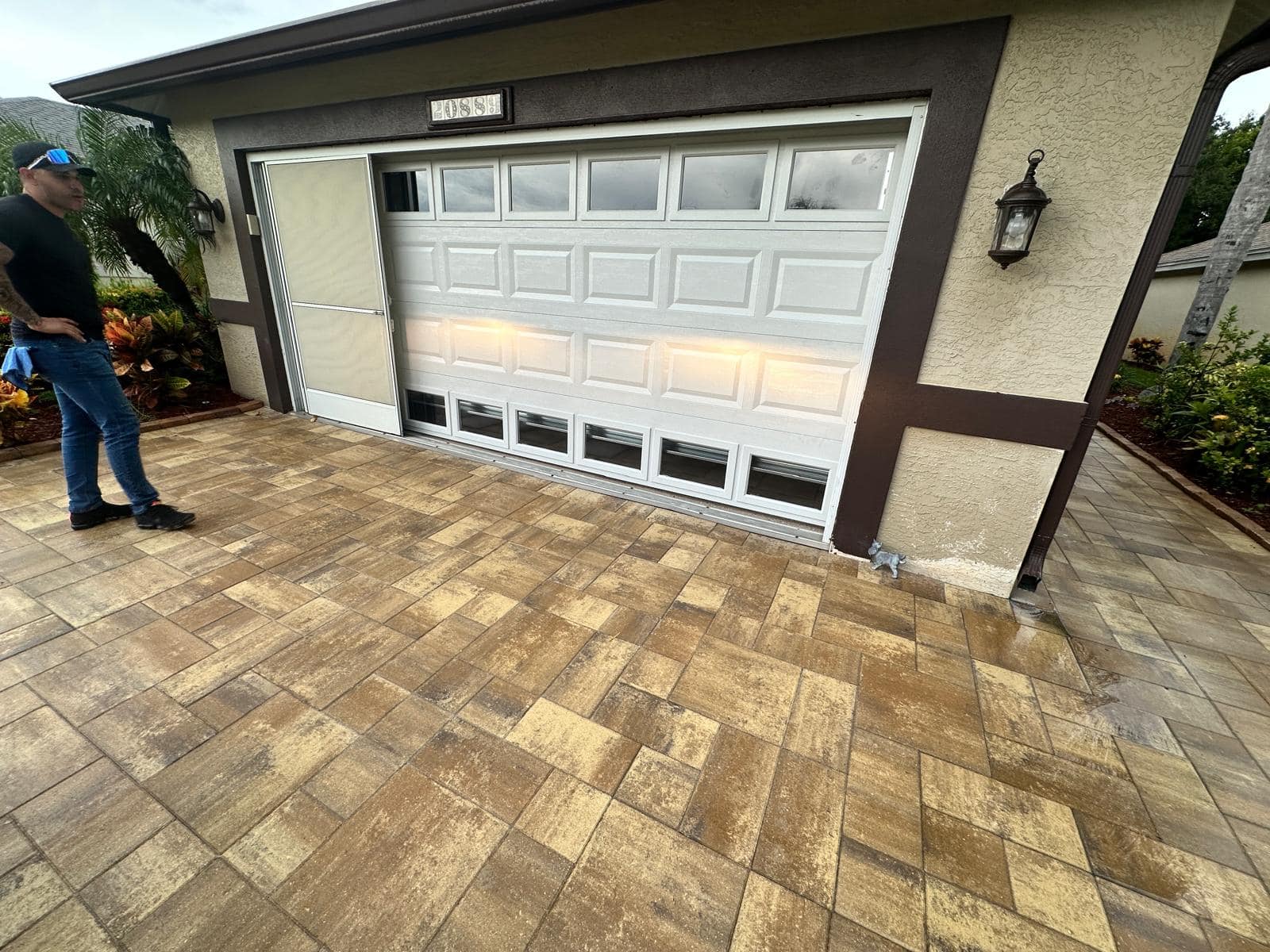 Richard Butrim, wearing a black shirt, blue jeans, and a cap, stands on a patterned stone driveway in front of a beige house with decorative outdoor lights and a partially raised white garage door for job 5146.