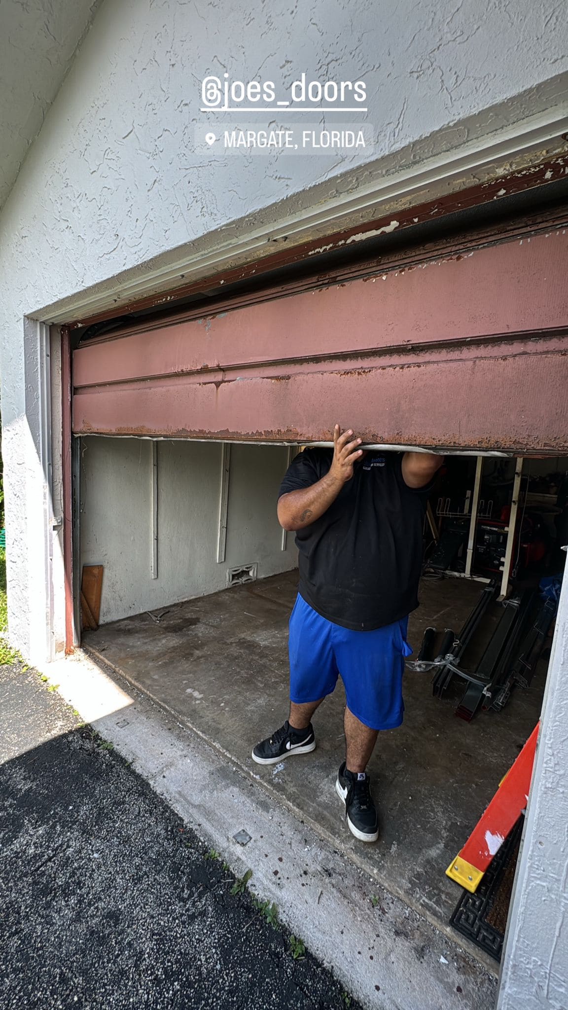 Dwayne Adams, in a black shirt and blue shorts, lifts a partially open brown garage door—Job 5441—at a Margate, Florida home. Tools and equipment are visible inside the garage, with part of his face obscured by the door.