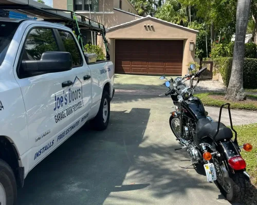 A white service truck labeled "Joe's Doors Garage Door Services" is parked in a driveway next to a black motorcycle. In the background, a two-story house features a brown garage door, palm trees, and reliable repair services.